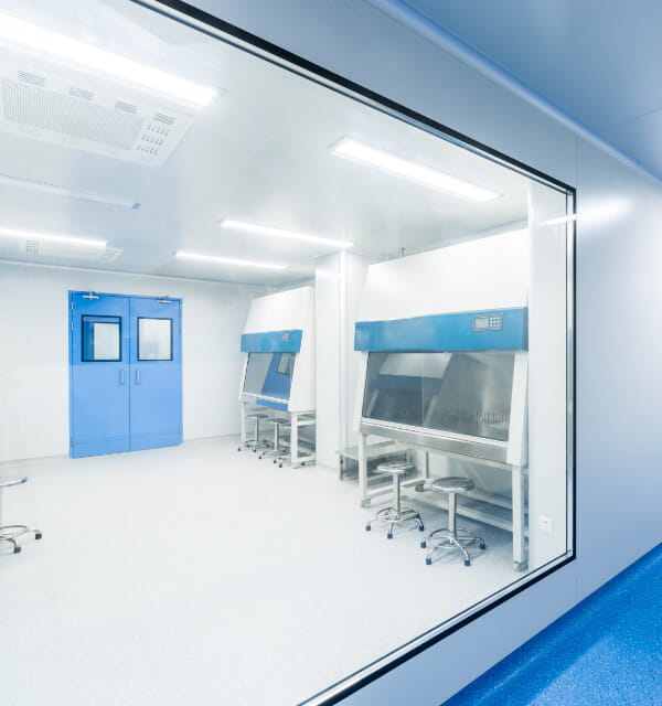 looking through a window into a cleanroom with blue double doors and rolling stools